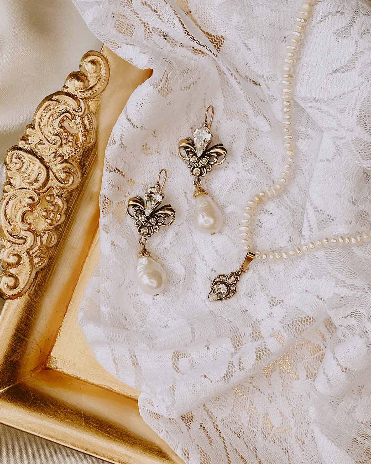 Pearl and crystal bridal jewelry arranged on lace beside an ornate gold mirror